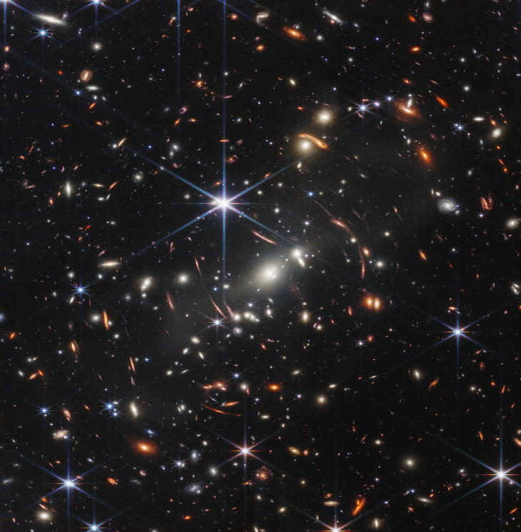 Космический телескоп НАСА им. Джеймса Уэбба получил самое глубокое и четкое инфракрасное изображение далекой Вселенной на 2022 год, сообщили в НАСА. Это изображение скопления галактик SMACS 0723 изобилует деталями. Тысячи галактик, в том числе самые тусклые объекты, когда-либо наблюдавшиеся в инфракрасном диапазоне, впервые попали в поле зрения «Уэбба».

Изображение называется “Первое глубокое поле Уэбба”. Подобные глубокие поля раньше делались с помощью телескопа Хаббл, но это наиболее глубокое, четкое и детализированное изображение ранней вселенной в инфракрасном диапазоне на сегодняшний день. 

Это глубокое поле, полученное камерой ближнего инфракрасного диапазона «Уэбба» (NIRCam), представляет собой композицию, сделанную из изображений на разных длинах волн, общей продолжительностью 12,5 часов. Эта глубина превышает максимальные возможности «Хаббла».

На изображении показано скопление галактик SMACS 0723, каким оно было 4,6 миллиарда лет назад. Объединенная масса этого галактического скопления действует как гравитационная линза, увеличивая гораздо более далекие галактики за ней. Камера NIRCam «Уэбба» позволила четко сфокусировать эти далекие галактики — у них есть крошечные, слабые структуры, которые никогда раньше не наблюдались, включая звездные скопления и диффузные детали. Исследователи скоро начнут узнавать больше о массах, возрасте, истории и составе галактик, поскольку «Уэбб» ищет самые ранние галактики во Вселенной.

