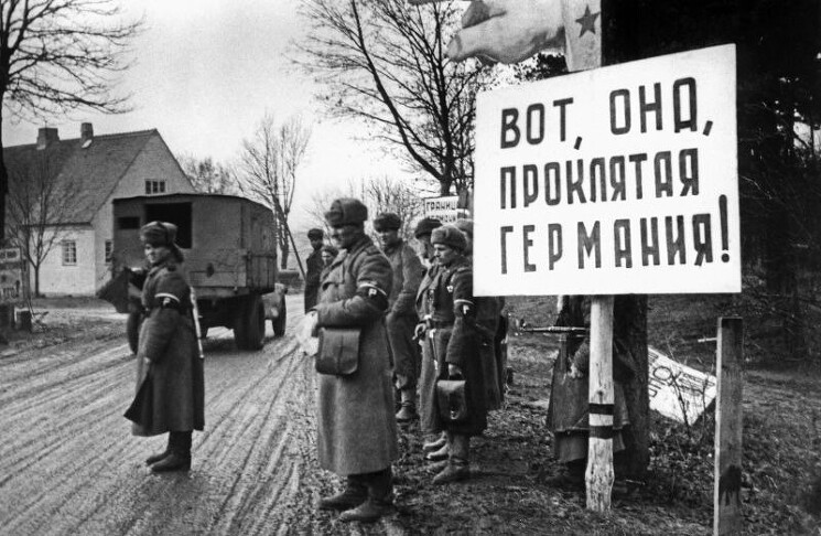 Советские регулировщики у плаката «Вот, она, проклятая Германия!» в Восточной Пруссии. Декабрь 1945 г.
